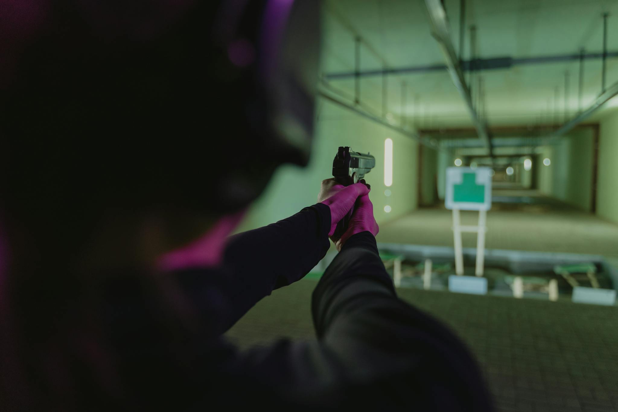 An individual targets a silhouette at an indoor shooting range using a handgun.
